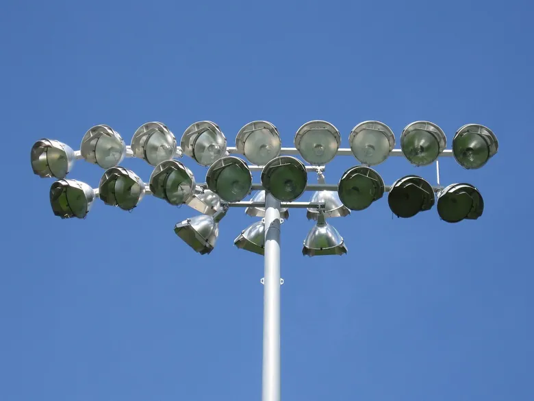 Cabeça de um poste de iluminação com cerca de vinte e cinco projetores, apagados, contra um céu azul